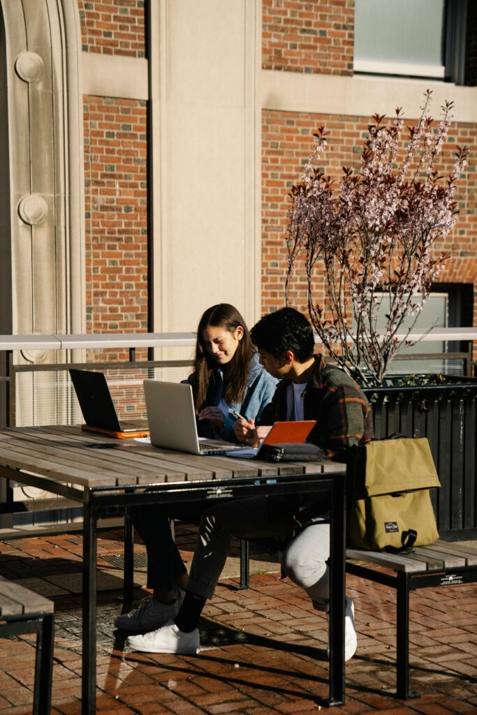 Young adults studying with laptops on a campus outdoor table, embracing technology and learning.