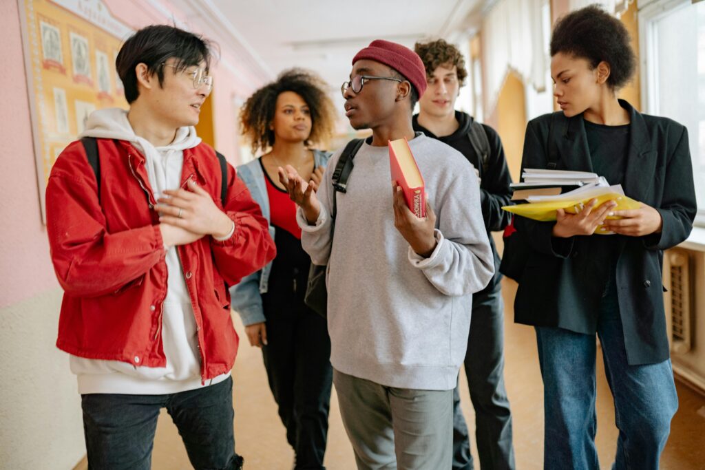 pexels-photo-8199164-8199164 A group of diverse students walking and talking in a school corridor, carrying books and folders.